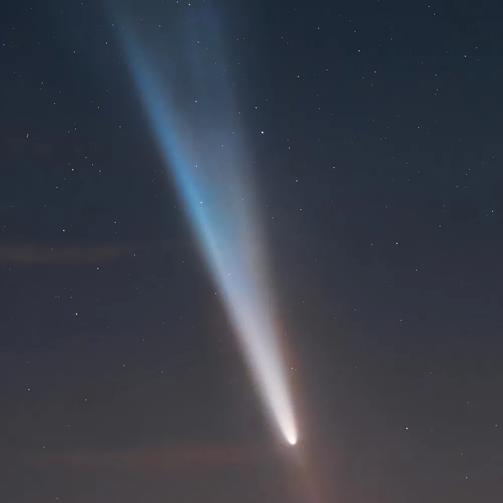 Cometa com uma cauda larga e azulada, ao crepúsculo