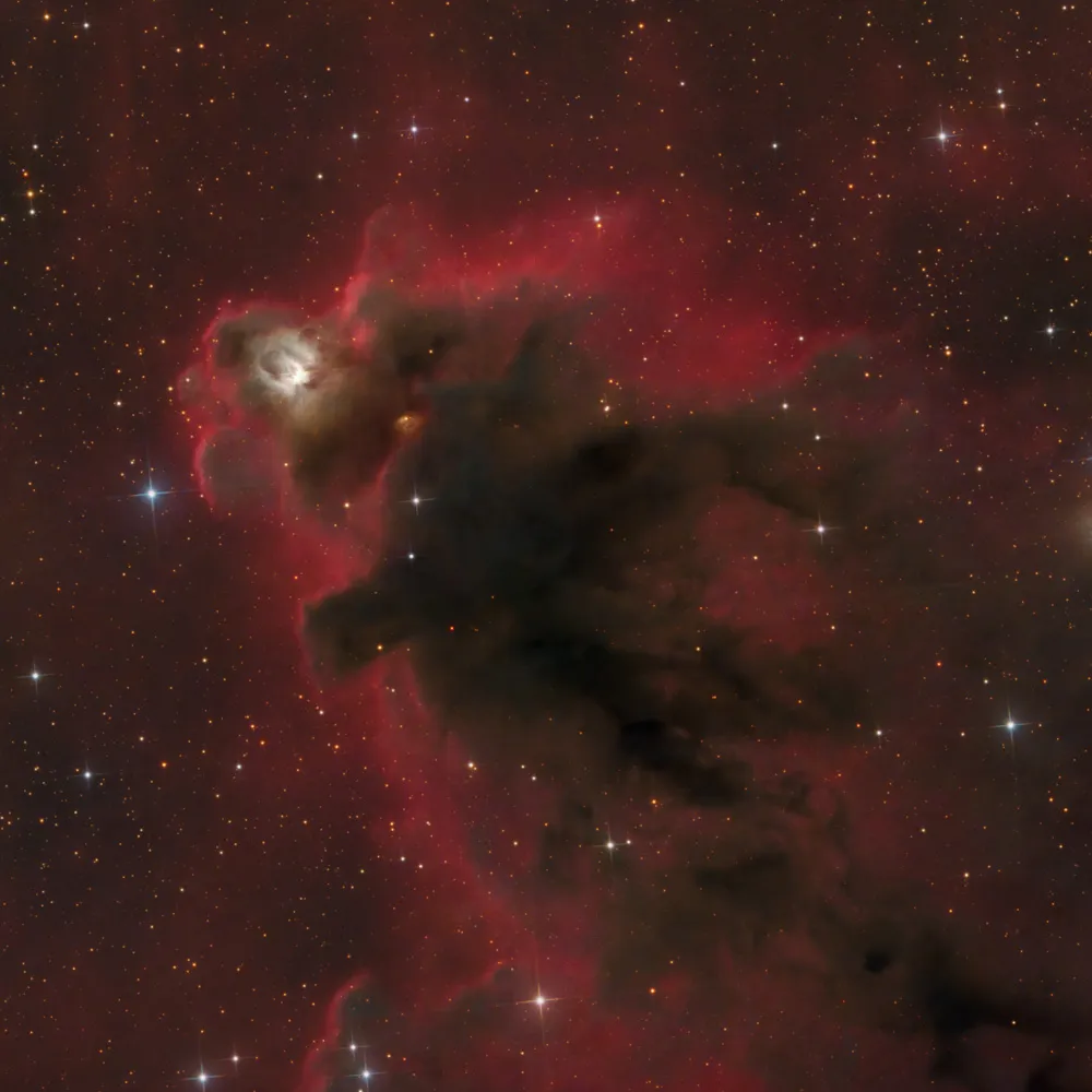 Nebulosa escura Boogeyman recortada contra nebulosidade vermelha, em Orionte